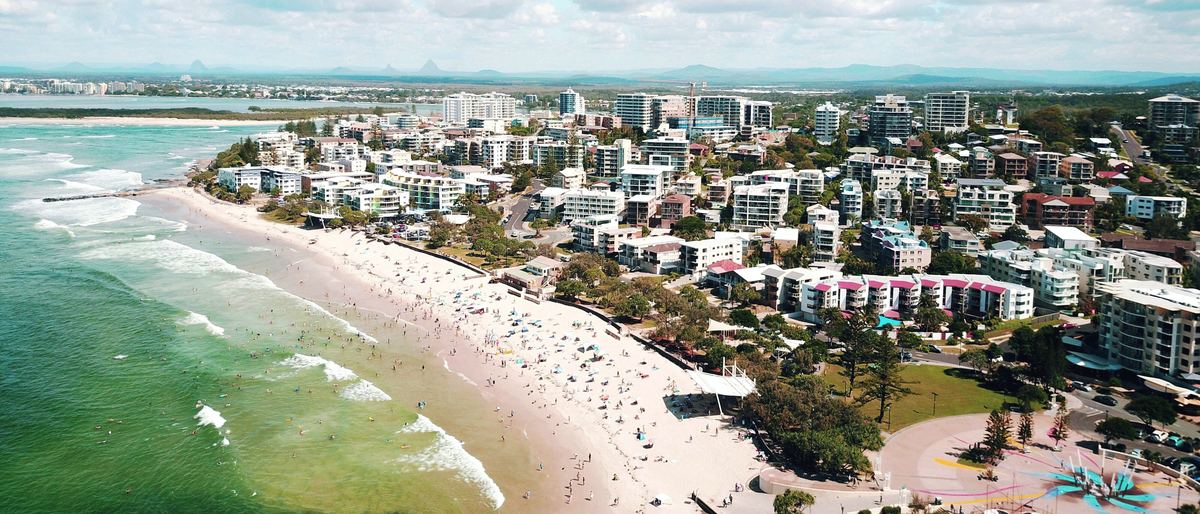 Aerial view of Kings Beach, Caloundra: the beach, the foreshore park and the apartments and houses behind it.
