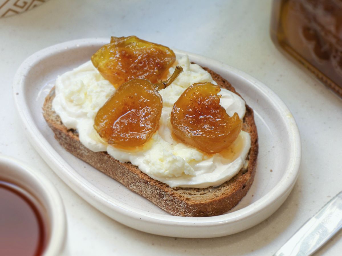 A slice of rye on a small white plate, spread thick with ricotta and topped with poached figs.