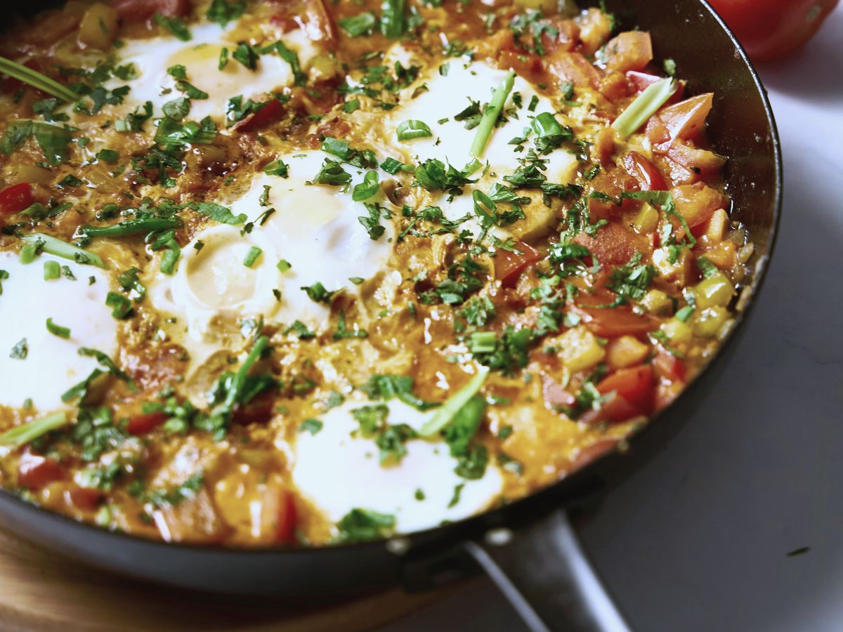 Shakshuka in a black pan: eggs set in peppers and tomato, scattered with chopped herbs.