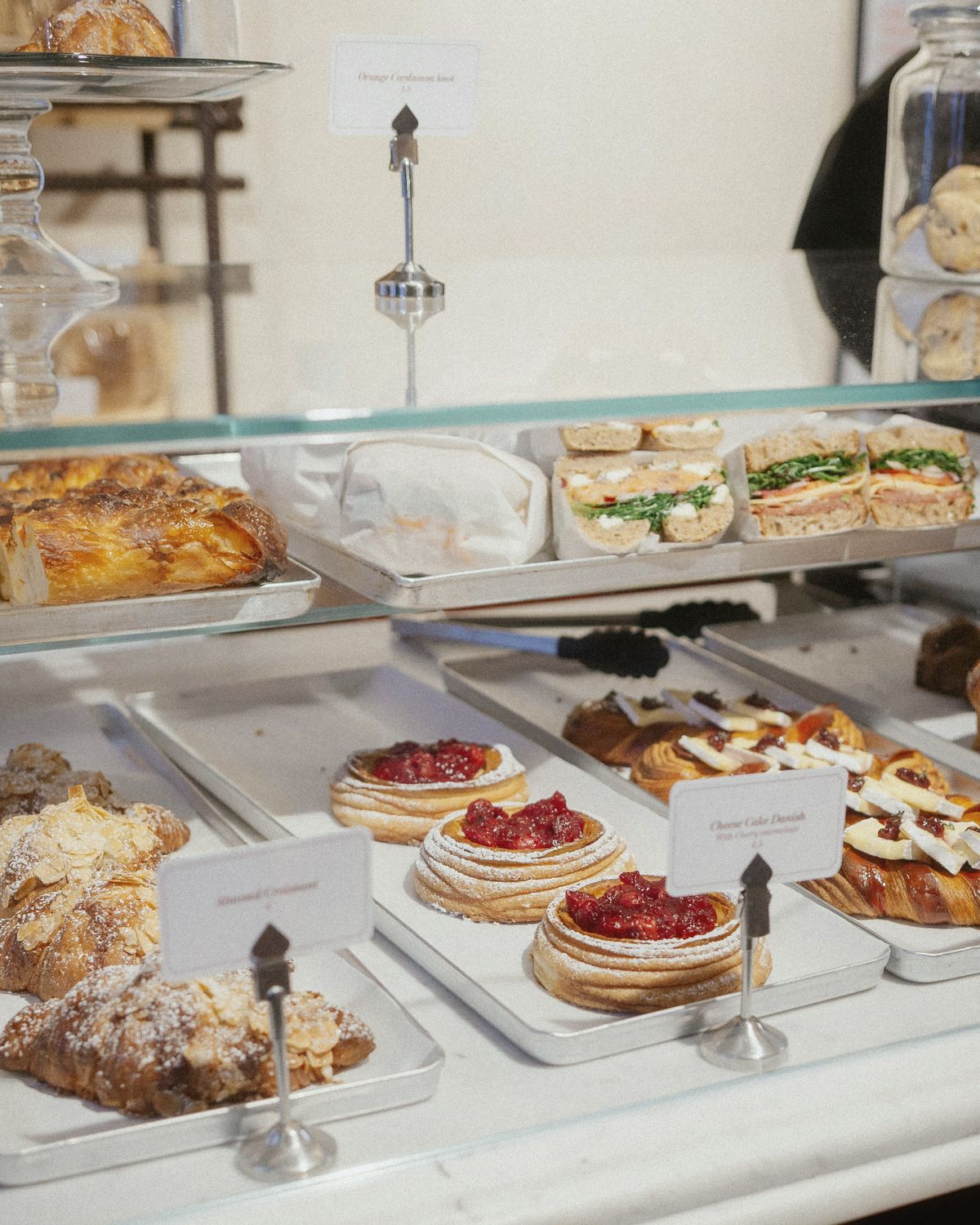 The pastry cabinet first thing: almond croissants, berry tarts and wrapped sandwiches behind the glass, each with a handwritten card.