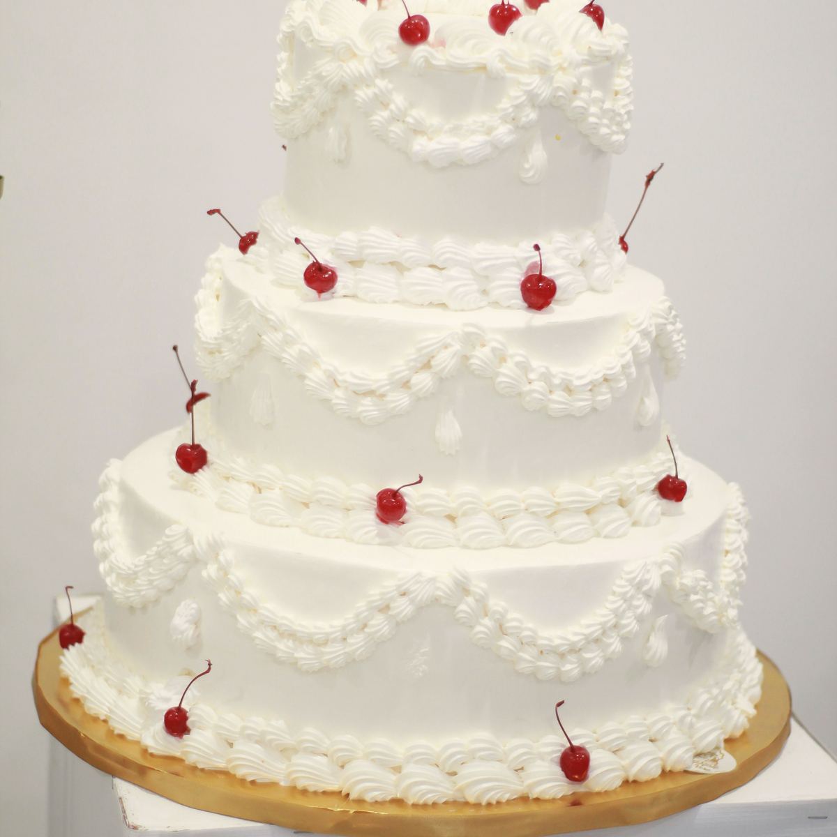 A three-tier white cake piped with beads and topped with cherries.
