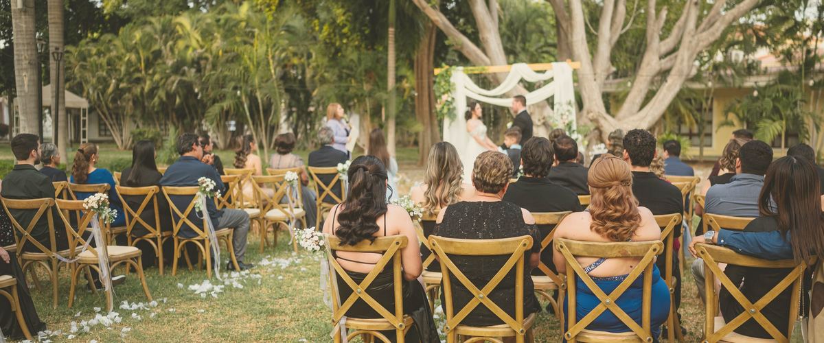 Guests on timber chairs watching the vows at the flower arch, seen from the back row, printed in two inks.