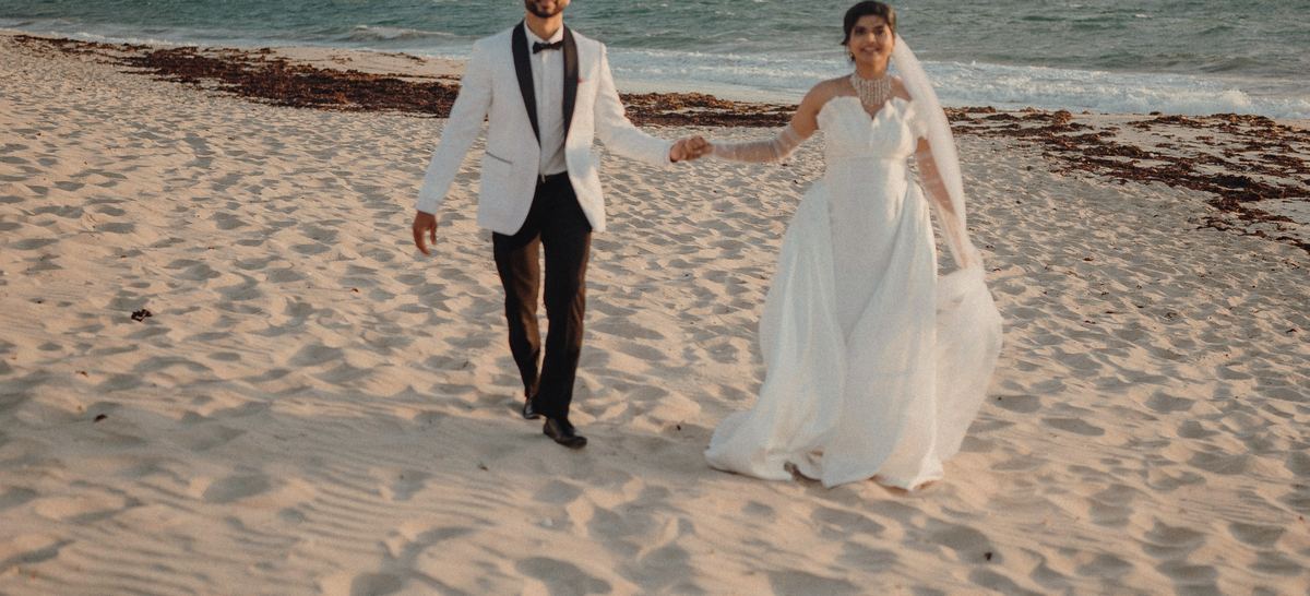 Anouk and Ben walking hand in hand across the pale sand below the lookout.