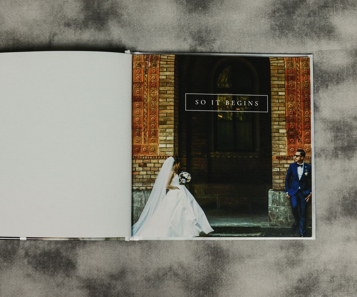An open lay-flat album on a grey cloth, one wedding photograph across the right-hand page.