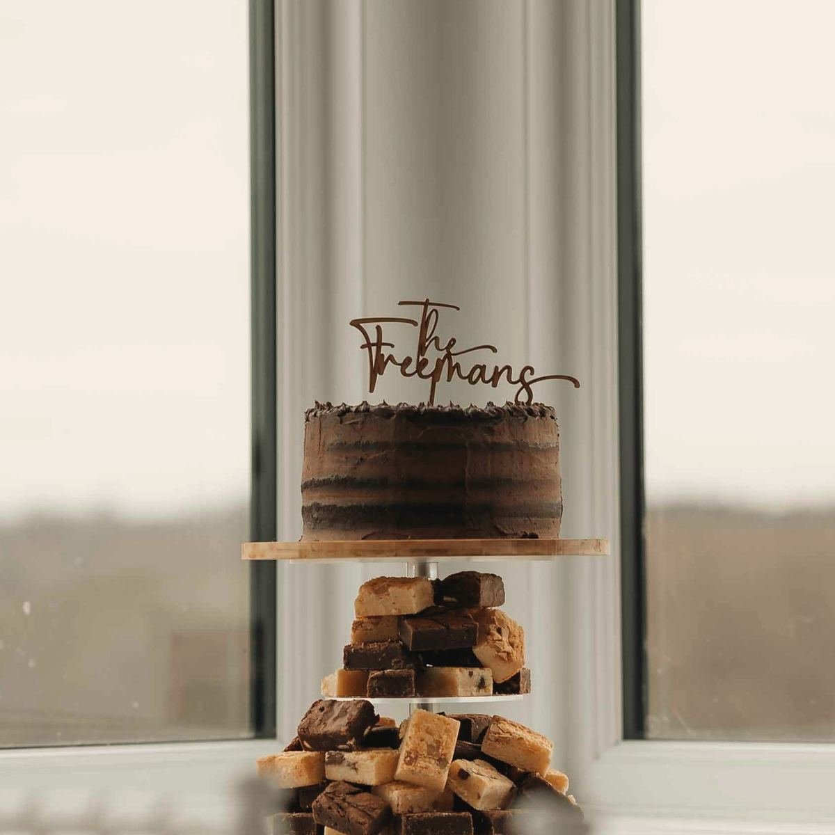 The cake on a stand by the window, a small topper on the top tier.