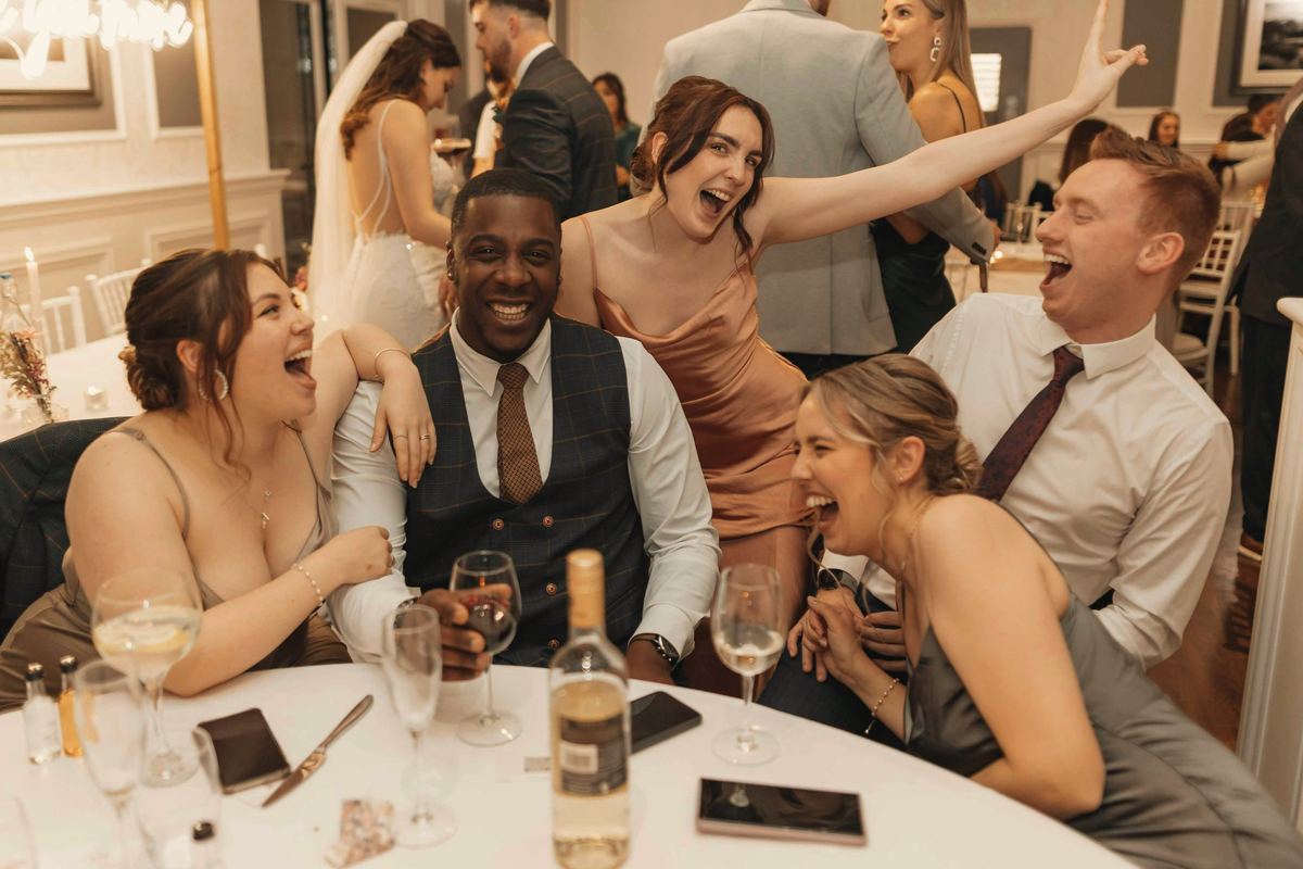 Guests at a round table in the hall, laughing so hard one of them is crying.