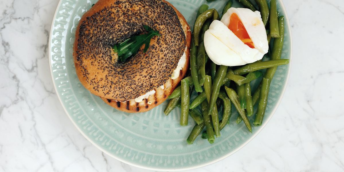 A poppy-seed bagel, green beans and a halved soft egg on a carved celadon plate.