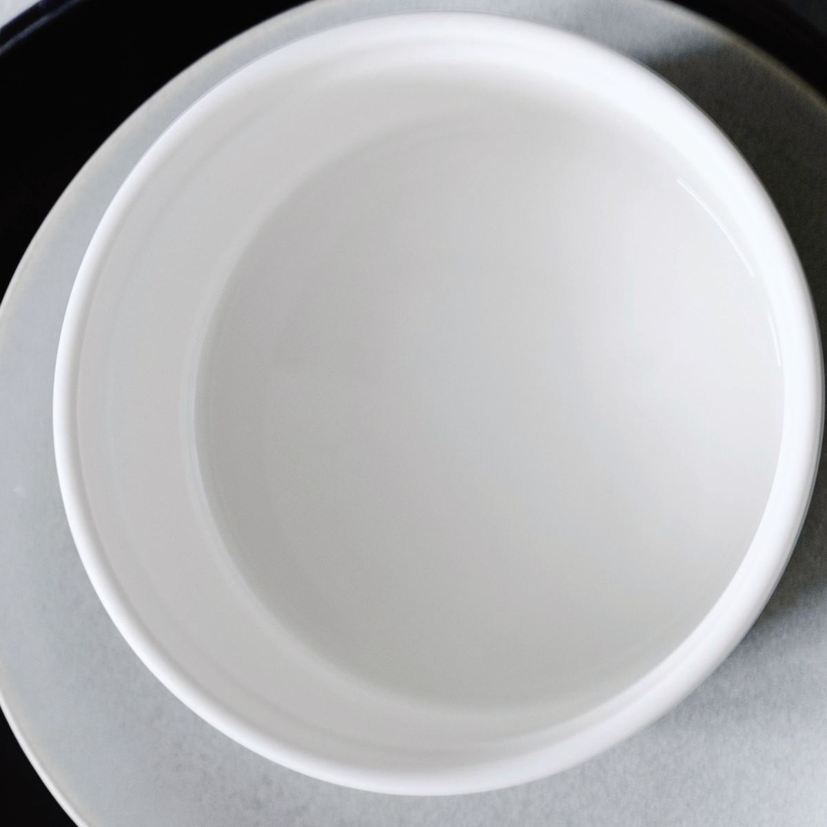 A satin white breakfast bowl from above, on a pale plate.