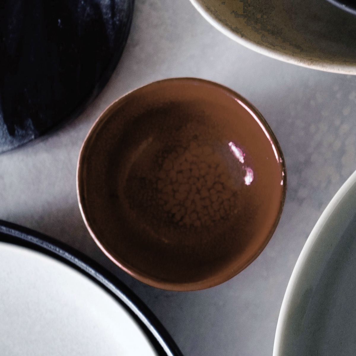 A small rust-brown bowl, glossy with darker speckle, on grey concrete.