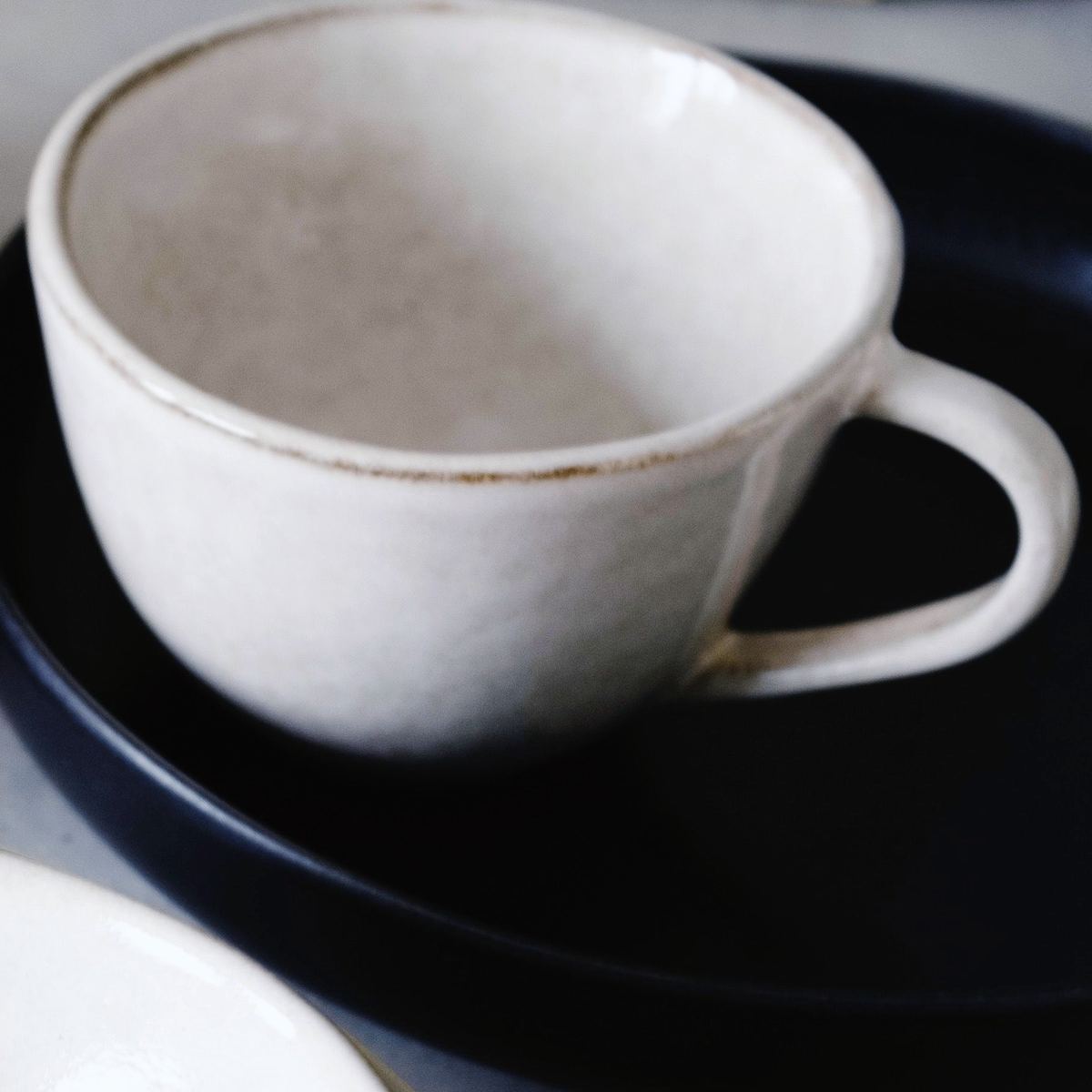 A white tea cup with a loop handle and a fine brown rim, on a dark plate.