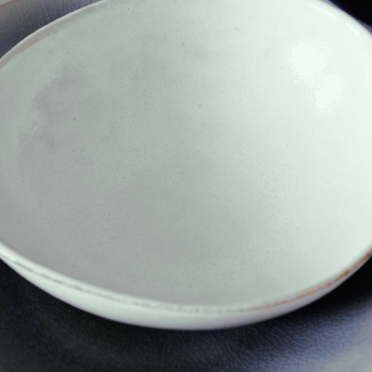 A shallow, slightly oval pale grey-green bowl with a fine brown rim.