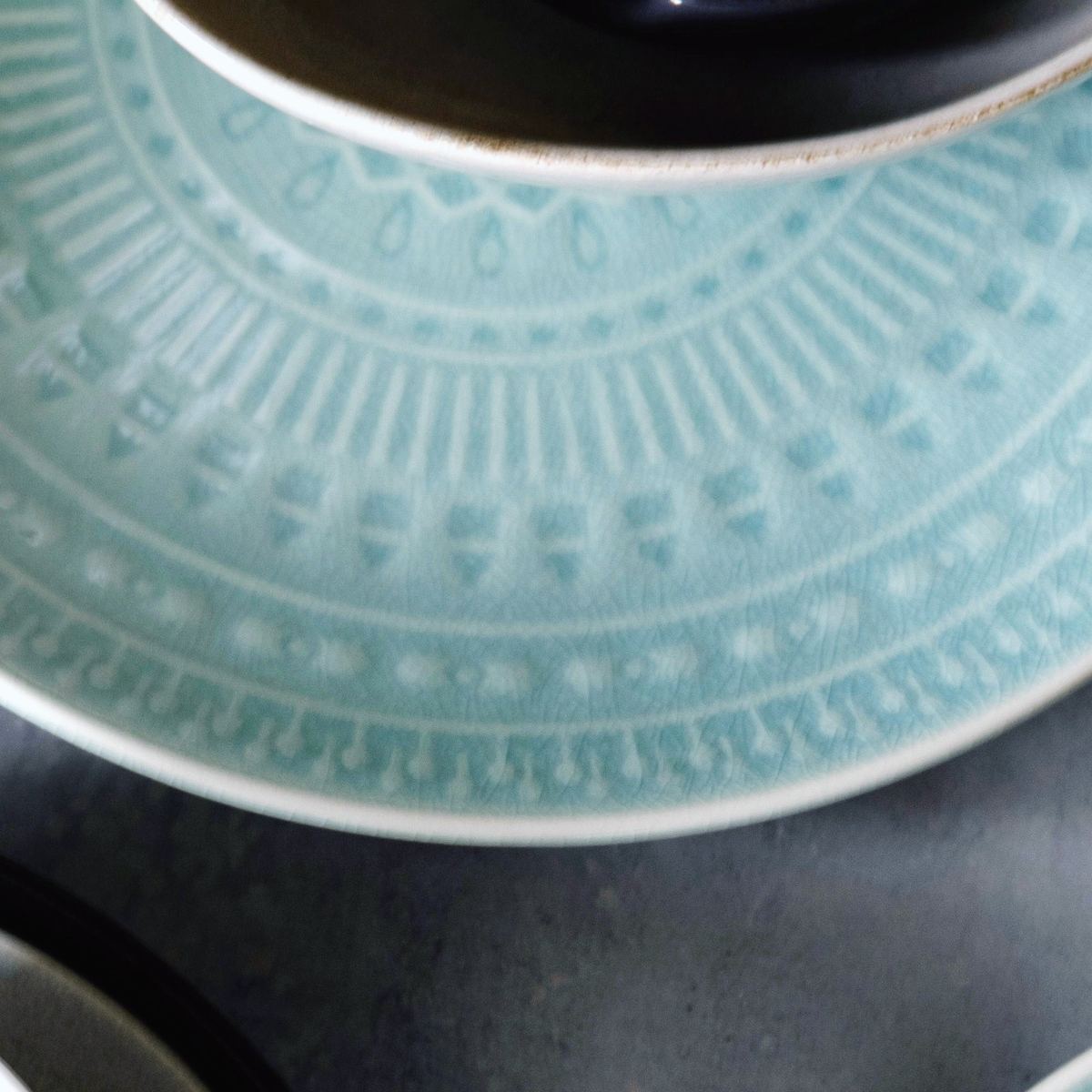 Close on the carved rim of a pale celadon plate, the pattern showing paler through the glaze.