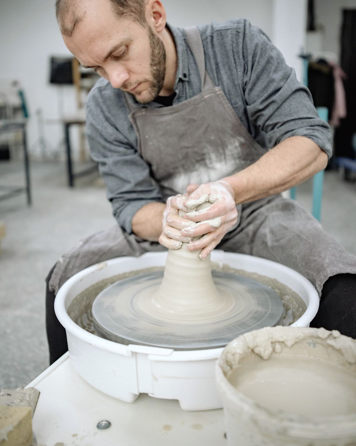 A potter centring a cone of clay on the wheel, both hands cupped around it.